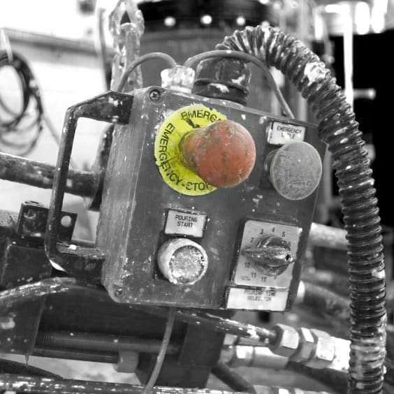 Black and white image of an bright red emergency stop button in an industrial setting